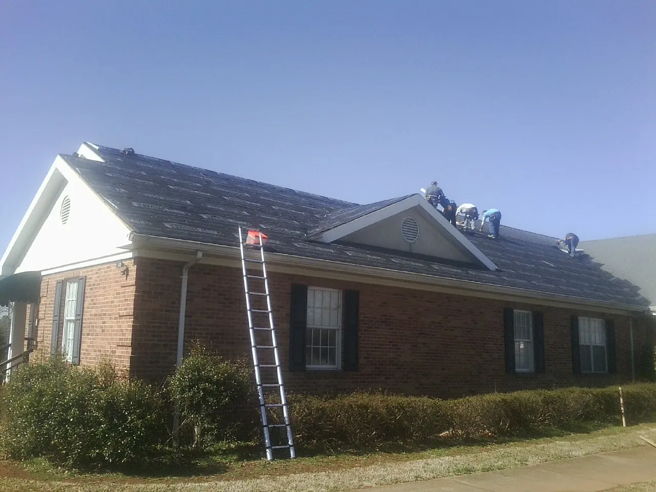 Crew tearing shingles off a brick ranch roof with a ladder set — Emergency Roof Repair work by our crew in Topanga