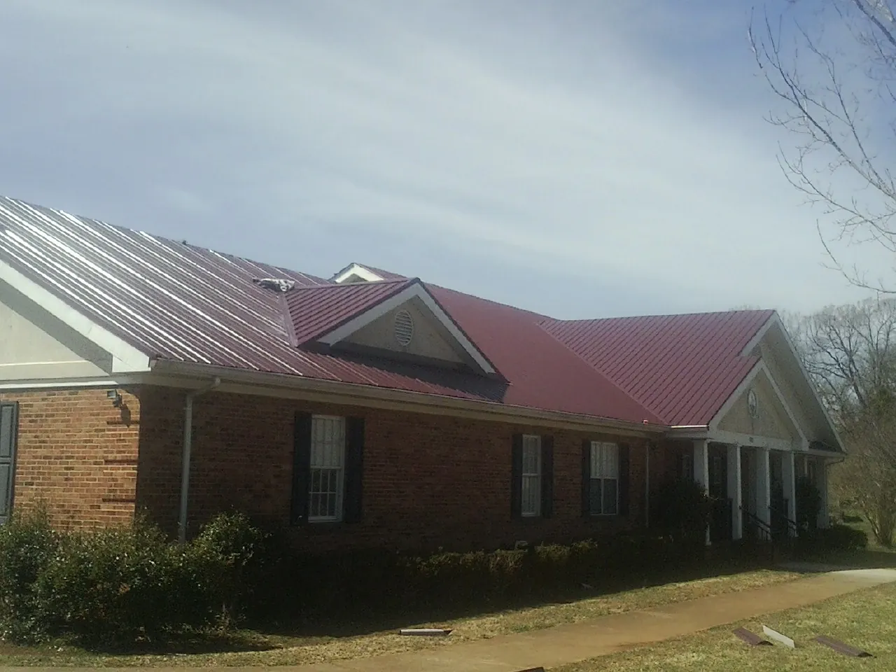 Red metal roof with gabled entries on a long brick building, from a Hail Damage Roof Repair job in Topanga
