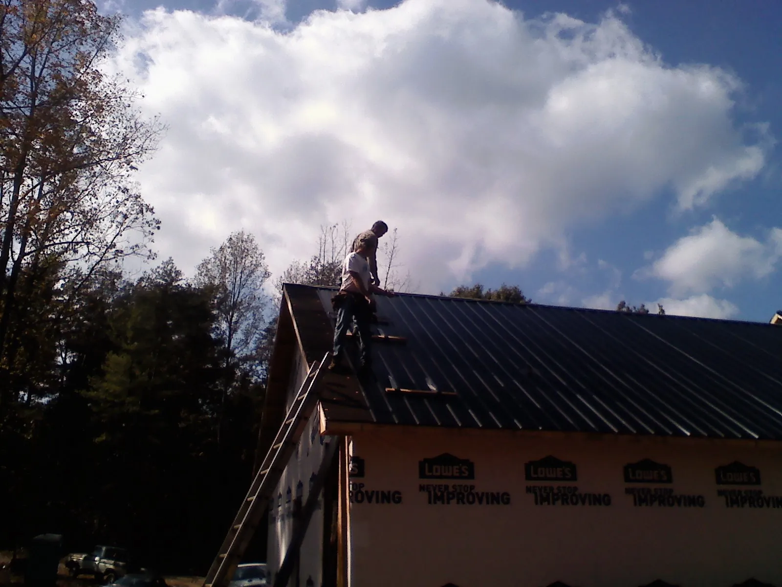 Roofer fastening dark metal panels high against a cloudy sky, from a Roof Inspection job in Topanga