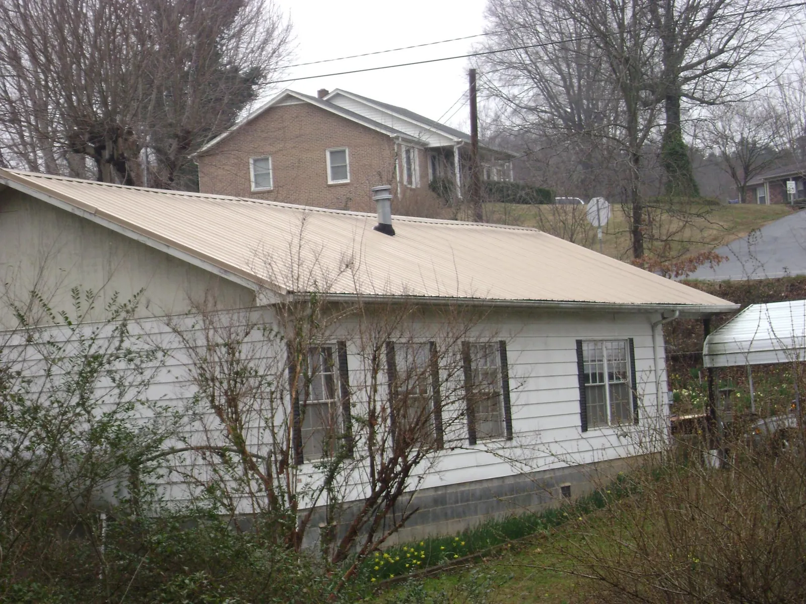 Tan metal roof on a white sided house set into a hillside — Commercial Roofing by Roofing Brothers in Topanga